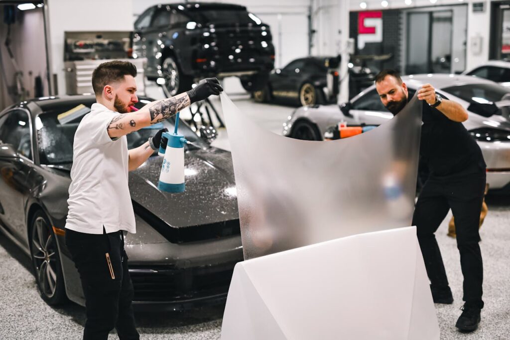 Two men working in garage applying protective film on a luxury car.